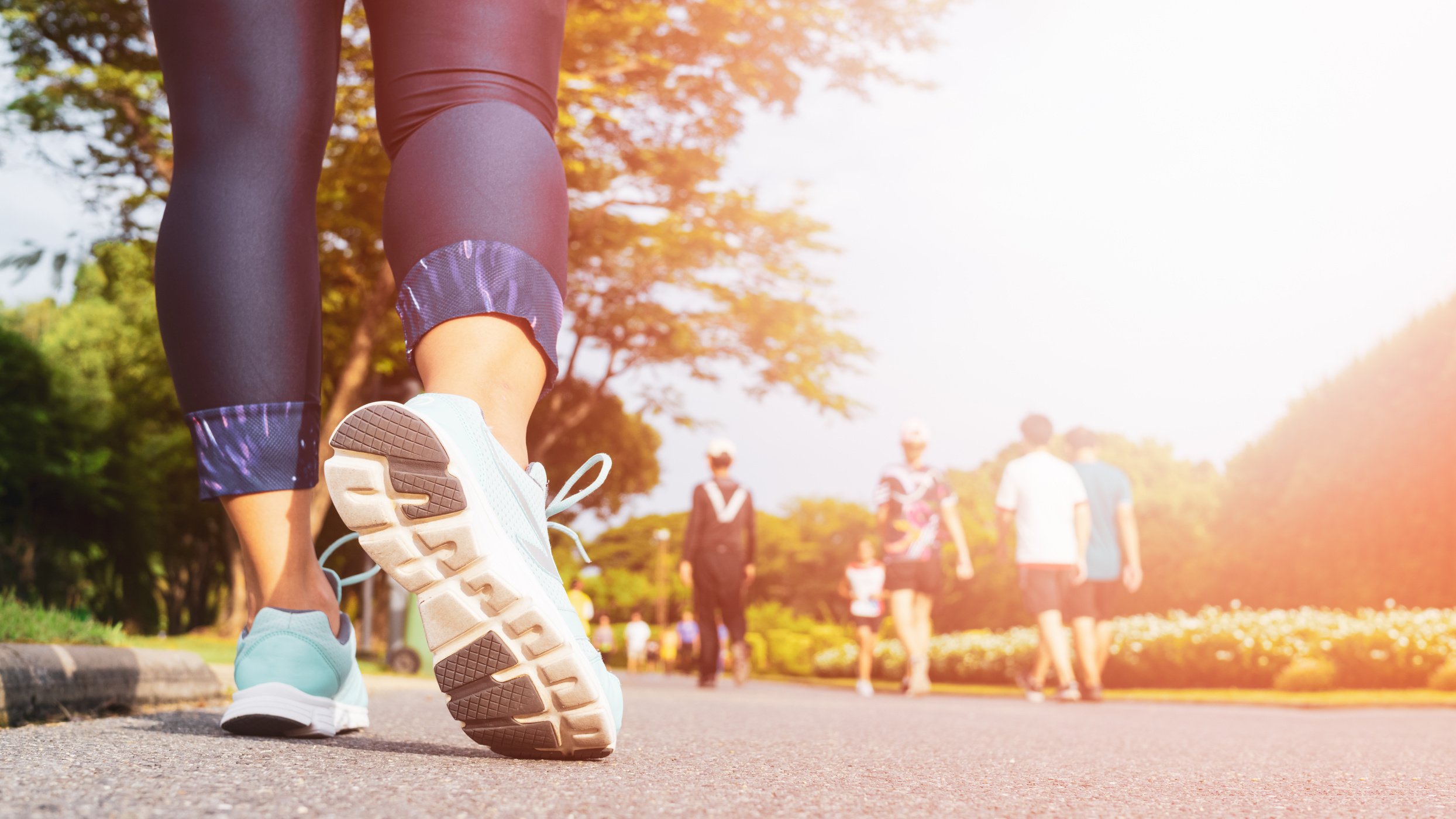 Young fitness woman legs walking with group of people exercise walking in the city public park in morning.